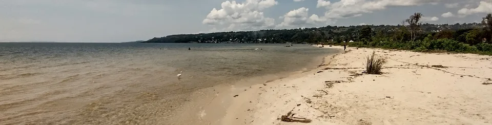 A long sandy shore at Bukoba curves beside Lake Victoria toward a green hillside.