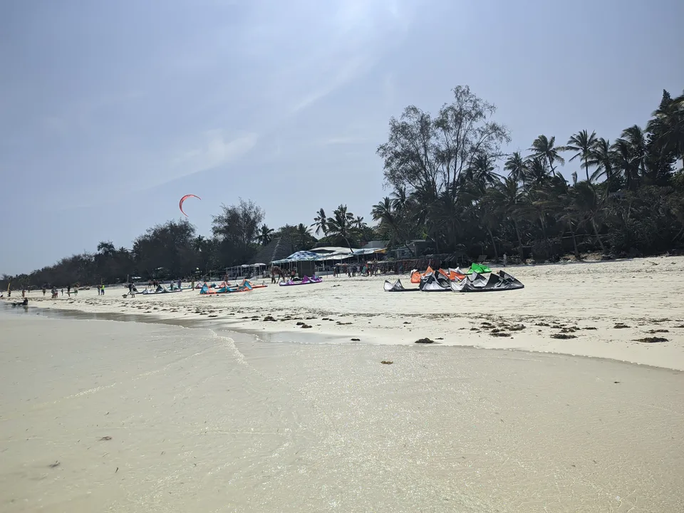 Pale sand and shallow water at Diani, with colorful kites and palms along the beach.