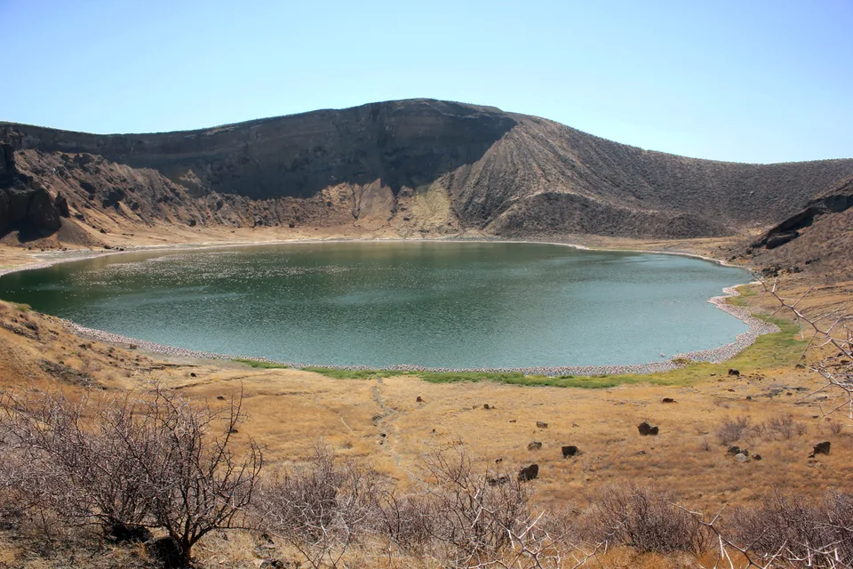 Green crater lake enclosed by dry volcanic slopes on Central Island, with sparse thorn scrub in the foreground.