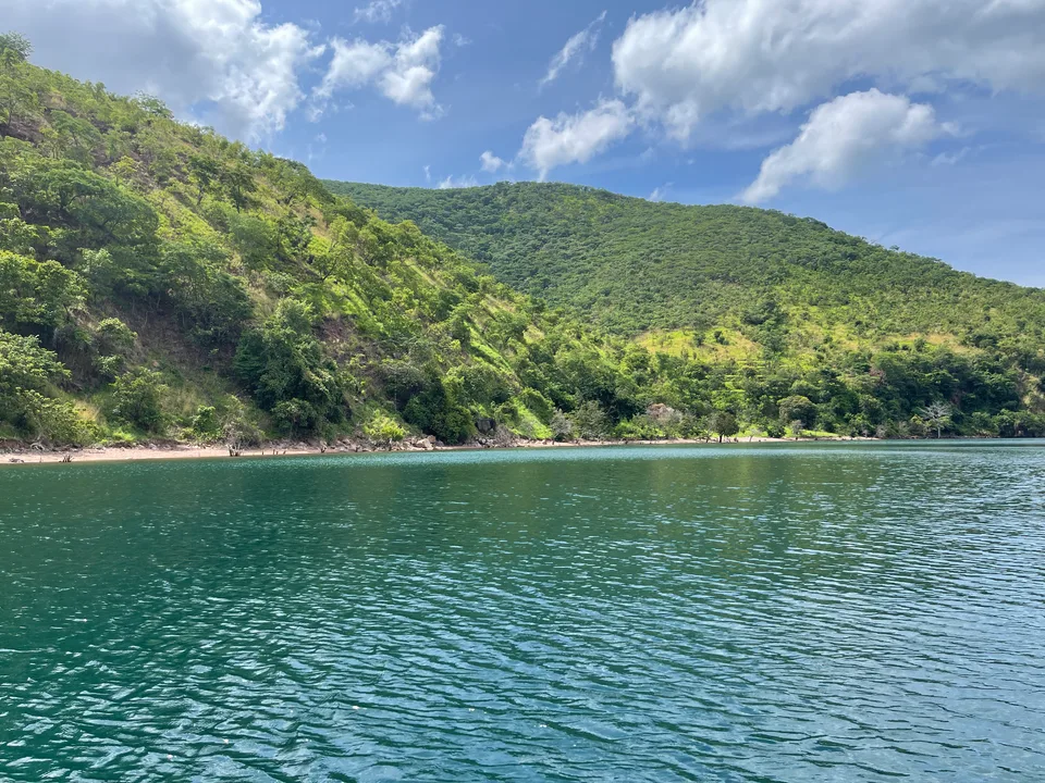 Green wooded hillside descending to a narrow Lake Tanganyika shore, seen across clear blue-green water.