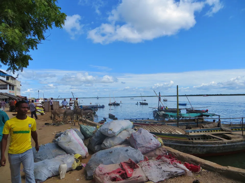 Boats and stacked sacks at Lamu’s working waterfront, with people and donkeys beside the shore.