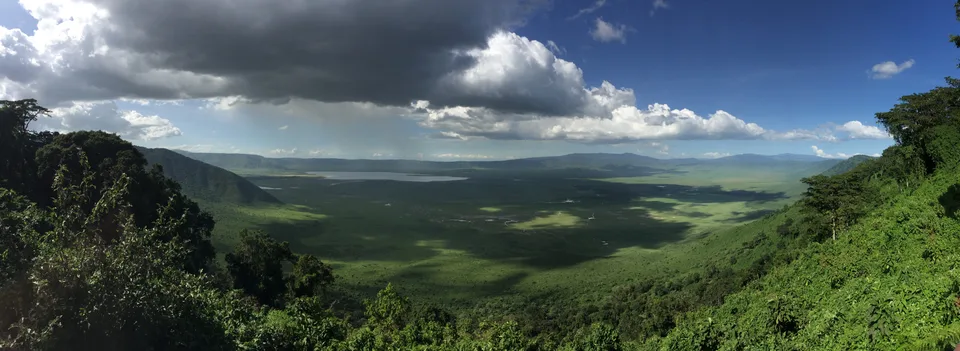 A wide view over Ngorongoro’s green crater floor, distant water and surrounding slopes beneath clouds.
