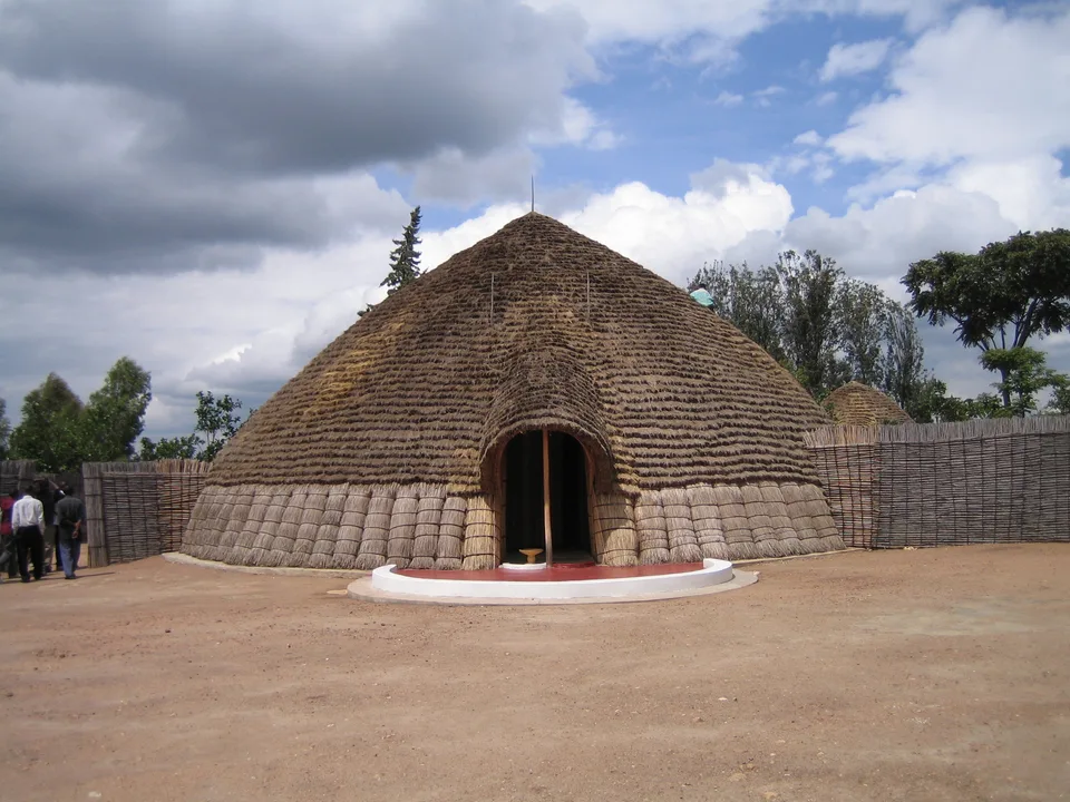 The rounded thatched reconstruction of the traditional King’s Palace at Nyanza, with a woven enclosure and visitors at the edge.