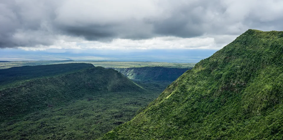 Steep green slopes and a broad valley at Mount Suswa beneath a low cloud layer.